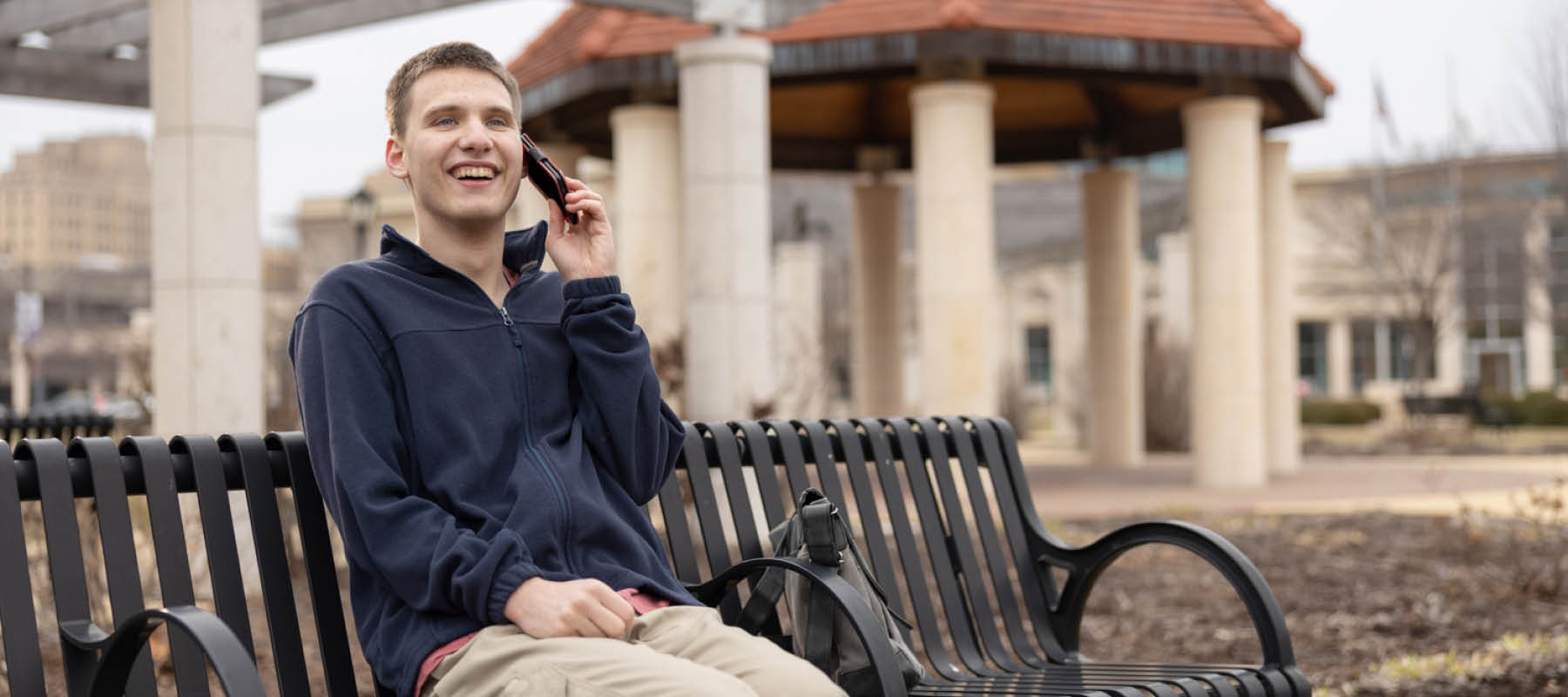 Young man with Autism sitting on bench talking on phone and smiling