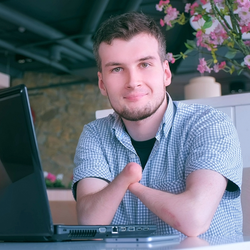 Young man with disability smiling at camera from computer in a café