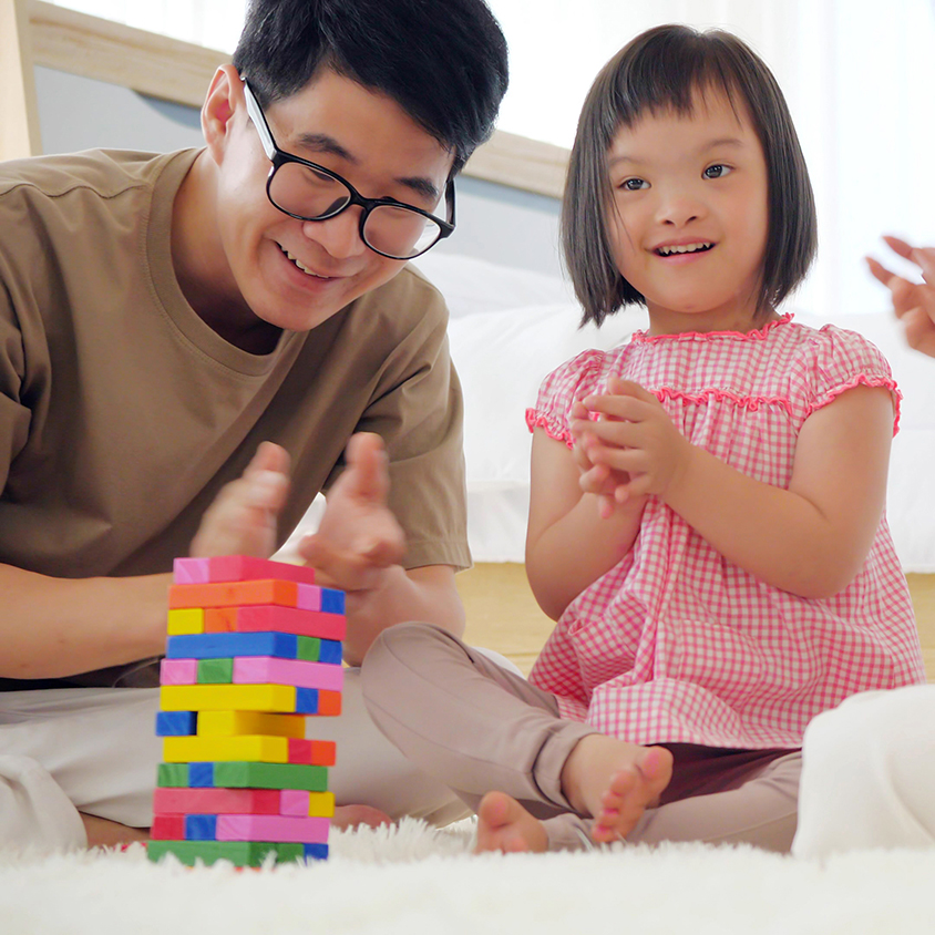 Little girl with Down syndrome smiling and playing on floor with parents